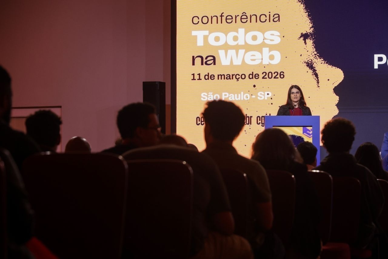 Cláudia Nascimento fala no púlpito da Conferência Todos na Web em frente à platéia.